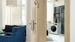 Ein modernes Wohnzimmer mit einem blauen Sofa, einer weißen Tür, die in einen Waschbereich mit Waschmaschine und Duschkabine führt.