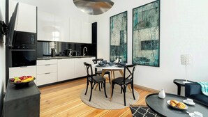 Eine moderne Küche mit weißen Schränken, einem Esstisch mit schwarzen Stühlen und einem schwarzen Couchtisch mit Gebäck.