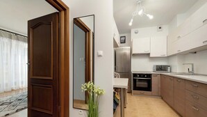 Cocina moderna con refrigerador, horno y microondas. Hay un comedor con mesa y sillas. Se ve una puerta de madera y un espejo.