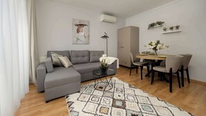 Una sala de estar moderna con un sofá gris, una mesa de comedor con sillas, un tapete estampado y una lámpara colgante.