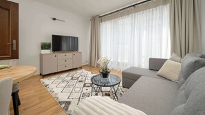 Una sala de estar moderna con un sofá, una mesa de centro de vidrio, un televisor sobre un mueble bajo y una alfombra estampada.
