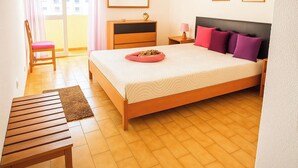 A bedroom with a bed, a wooden nightstand, a chair, a dresser, and a window with curtains. - Praia da Rocha 1 Bedroom Apartment With Balcony (Portimão)