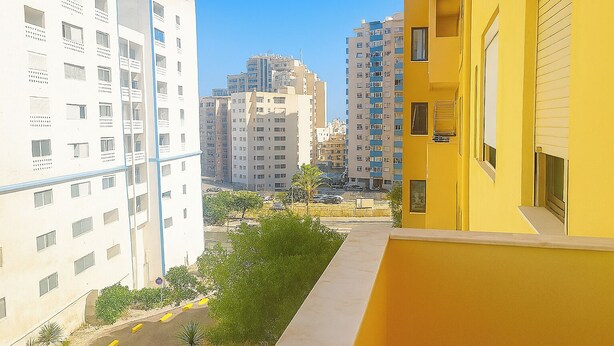 A residential area with high-rise buildings, a narrow street, and a yellow building on the right. - Praia da Rocha 1 Bedroom Apartment With Balcony (Portimão)