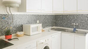 A modern kitchen with white cabinets, a microwave, a sink, and a washing machine. - Praia da Rocha 1 Bedroom Apartment With Balcony (Portimão)