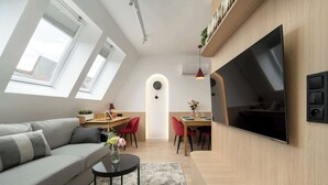 Un espacio habitable moderno con sofá, mesa de comedor, televisor y ventanas tipo tragaluz.