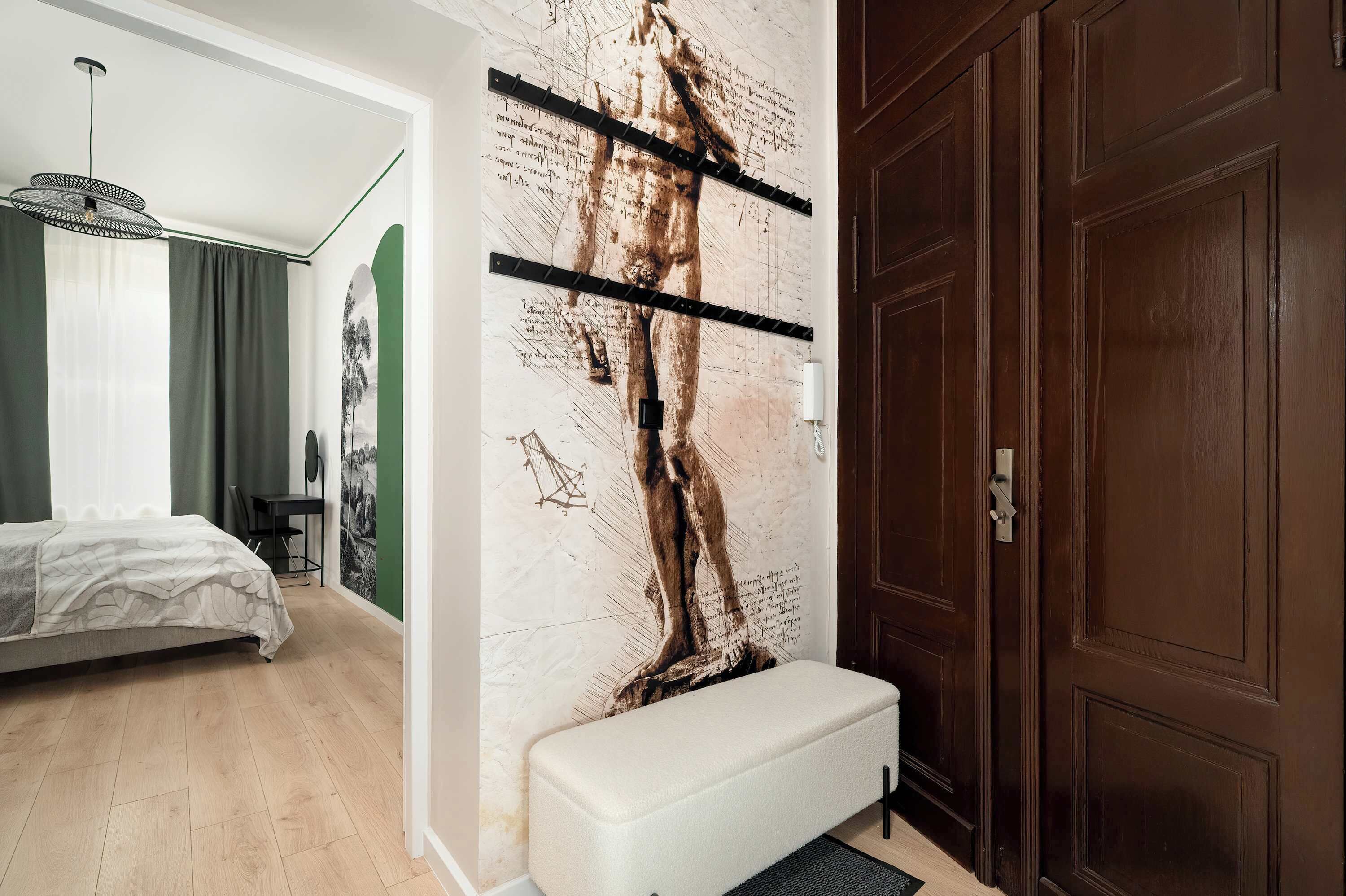 A bedroom with a bed, a bench, a wall with a large artwork, a door, and a hallway.