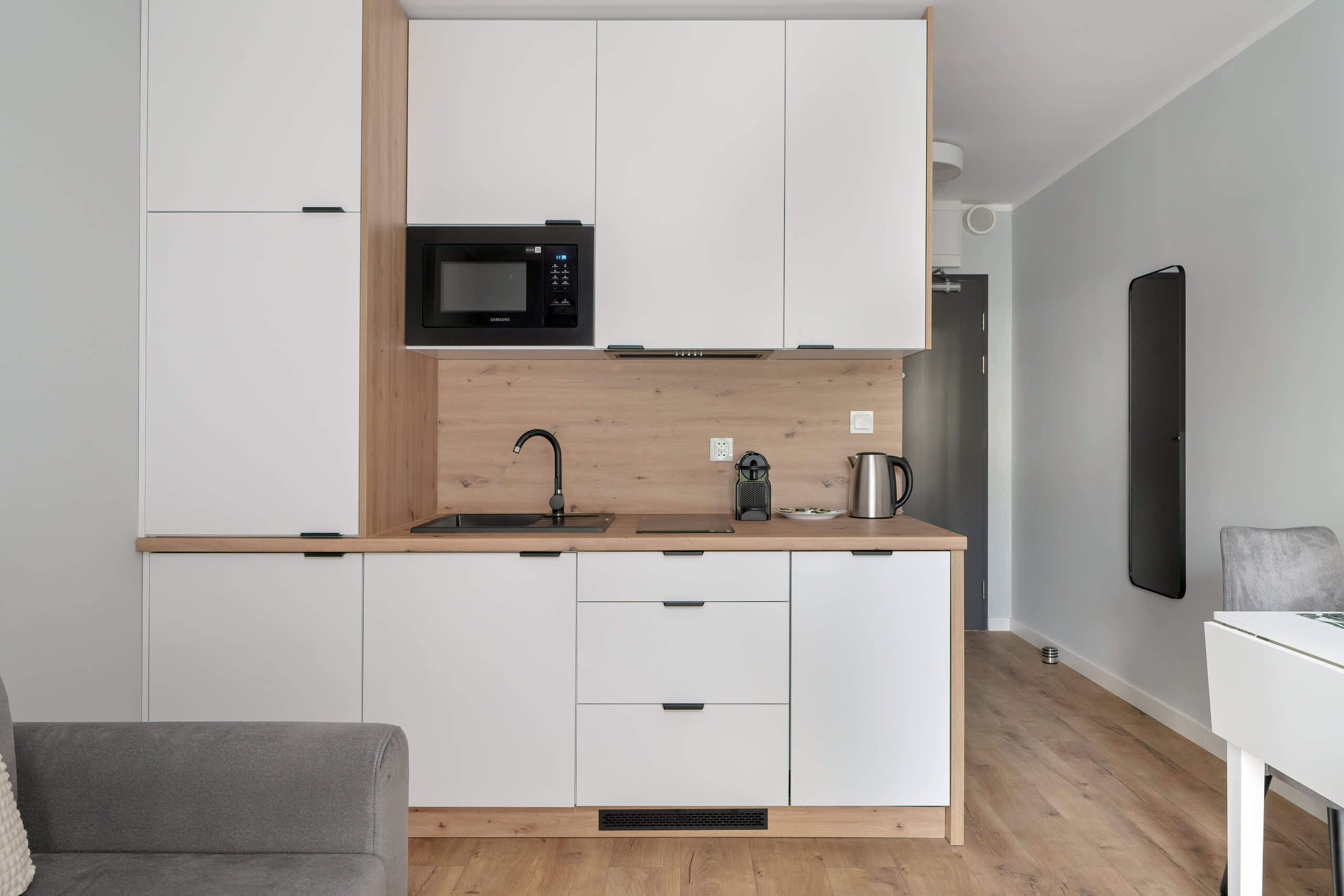 A compact kitchen with white cabinets, a microwave, a sink, and a coffee maker.