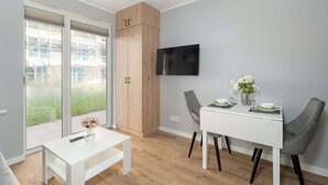 Een moderne eethoek met een witte tafel en stoelen, een houten kast en een aan de muur bevestigde televisie.