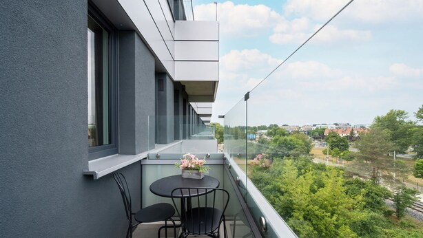 Ein Balkon mit Tisch und Stühlen, einer Blumenvase und Blick auf Grünflächen und Gebäude.