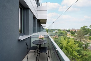 Un balcone con tavolo e sedie, un vaso di fiori e vista su spazi verdi ed edifici.