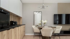 Eine moderne Küche mit integriertem Geschirrspüler, einem Essbereich mit rundem Tisch und Stühlen, einem großen Spiegel und einem flachbildfernseher an der Wand.