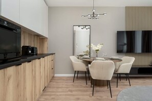 A modern kitchen with a built-in dishwasher, a dining area with a round table and chairs, a large mirror, and a flat-screen TV mounted on the wall.
