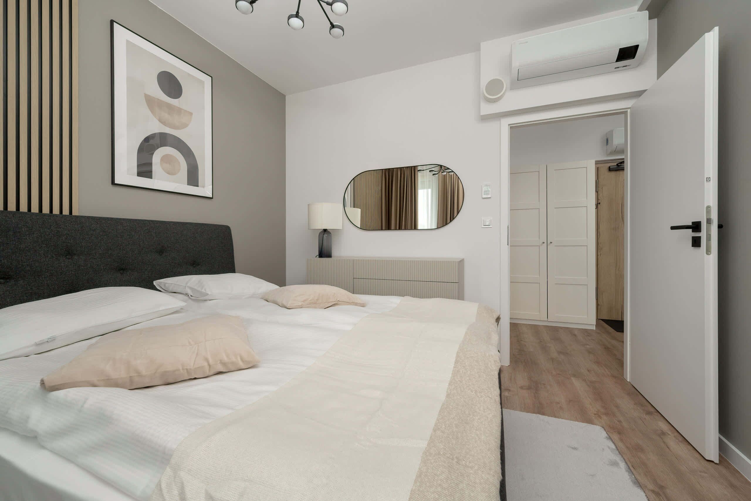 Un dormitorio moderno con cama, lámpara de noche, espejo y aire acondicionado.