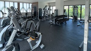 Uma academia com diversos equipamentos de ginástica, grandes janelas e teto alto.