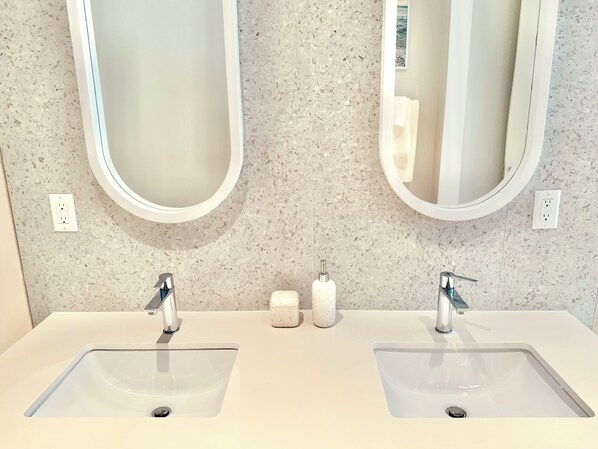 Un baño con dos lavamanos, cada uno con un espejo encima. Hay dos dispensadores de jabón en la encimera.