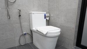 Un baño moderno con inodoro blanco, ducha de mano y conexión de agua visible.