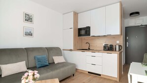 Un appartement moderne avec un canapé gris, une table à manger en bois, une cuisine dotée de meubles blancs et d’un four à micro-ondes, et deux tableaux encadrés accrochés au mur.