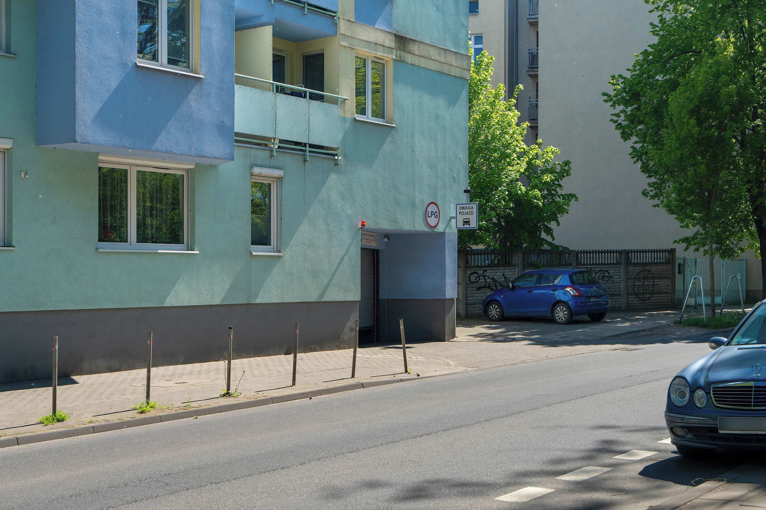 Ein mehrstöckiges Wohngebäude mit Balkonen, einem Verbotsschild und einem blauen Auto, das an der Straße geparkt ist.
