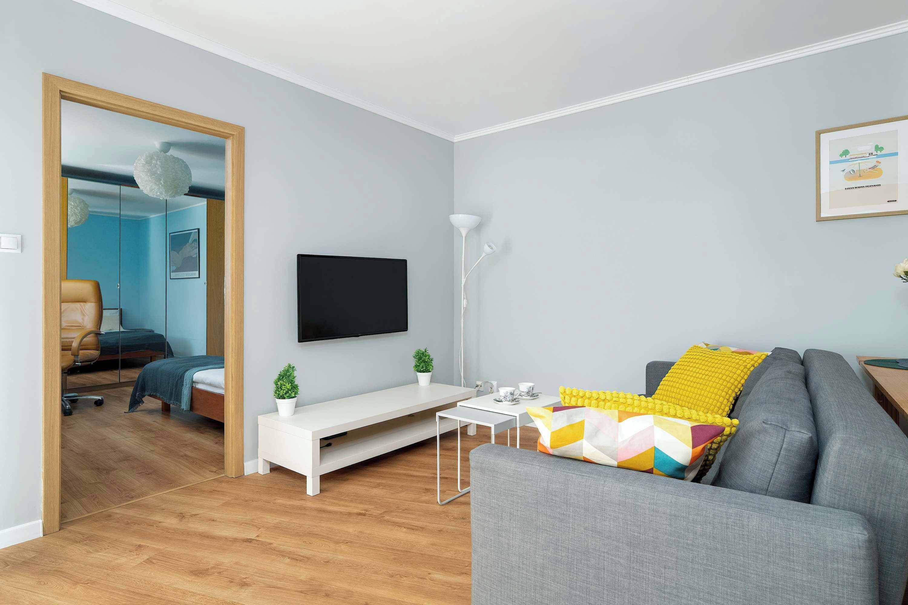 A modern living room with a grey sofa, a white coffee table, and a flat-screen TV mounted on the wall.