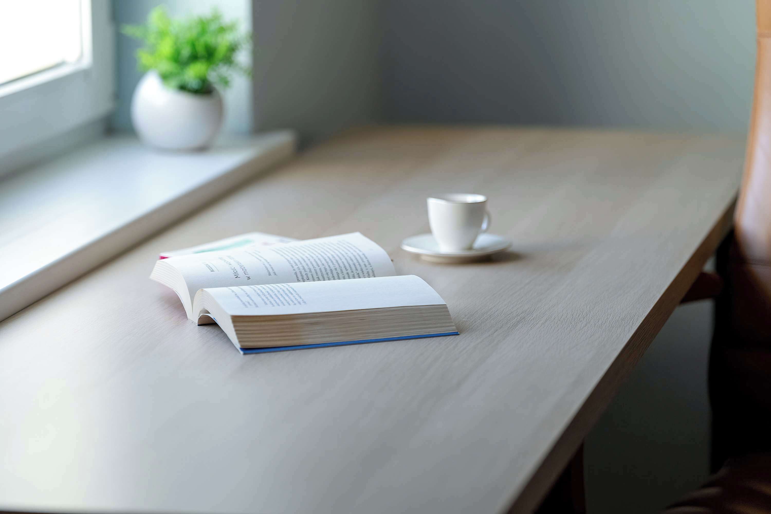 Ein Holztisch mit einem offenen Buch und einer weißen Tasse auf Untertasse.