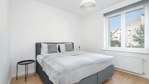 Un dormitorio con una cama, una mesita, una ventana y un radiador.