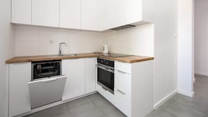Una cocina compacta con muebles blancos, encimera de madera, lavavajillas integrado y horno de acero inoxidable.