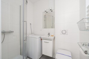 A bathroom with a glass shower enclosure, a washing machine, a sink, a toilet, and a mirror. - Poznan | Rycerska 5 | Spacious Apartment | Free Parking (Poznań)