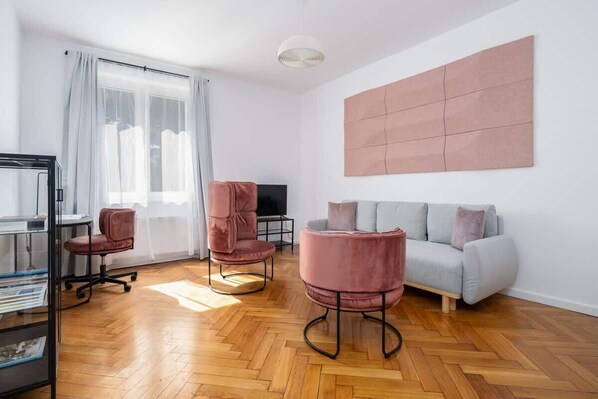 A modern living room with a wooden herringbone floor, a grey sofa, two pink armchairs, a glass cabinet, and a large abstract art piece on the wall. - Poznan | Rycerska 5 | Spacious Apartment | Free Parking (Poznań)