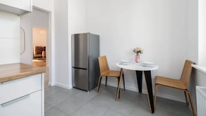 Una cocina moderna con armarios blancos, un refrigerador de acero inoxidable y una mesa redonda con dos sillas.