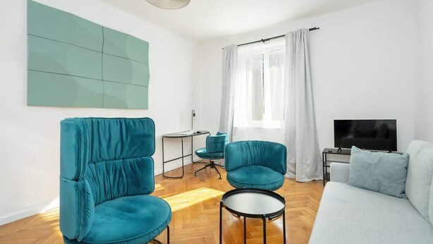 Una sala de estar moderna con un sofá, dos sillones, una mesita de centro, un televisor y un cuadro abstracto grande en la pared.