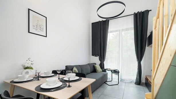 A modern, minimalist room with a dining table set for two, a sofa, and a staircase.