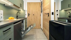 A narrow kitchen with a dishwasher, a wooden door, and a countertop with a cutting board and oranges.