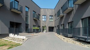 A modern building with a central courtyard, featuring a geometric pattern on the facade, balconies, and a paved walkway.