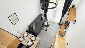 A modern living room with a sofa, a dining table set for two, and a staircase leading to an upper floor.