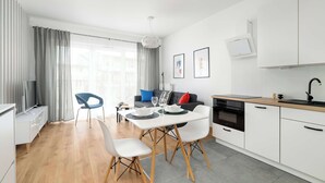 A modern kitchen with white cabinets, a dining area with a table and chairs, and a living area with a sofa and a TV.