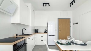 A compact kitchen with white cabinetry, a black countertop, and a dining area with a white table set for two.