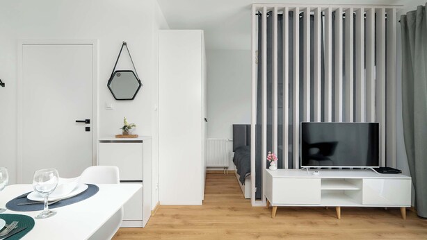 A modern living room with a white entertainment unit, a flat-screen TV, and a dining area with a table set for two.