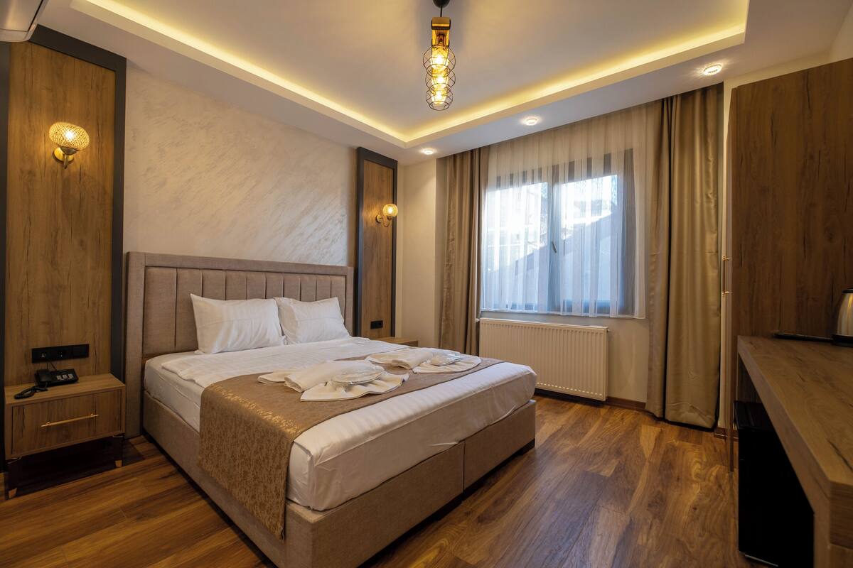 A modern hotel room with a large bed, bedside tables, a desk, and a window with curtains.