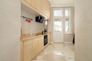 A compact kitchen with wooden cabinets, a built-in oven, a sink, and a small window.