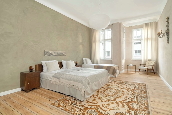 A bedroom with two beds, a nightstand, a lamp, a chair, and a patterned rug.