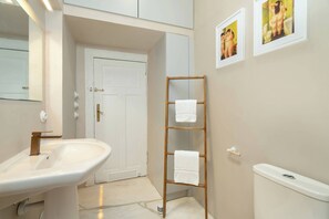 Un baño con un lavamanos blanco, un perchero de madera y un inodoro. Hay cuadros enmarcados en la pared.