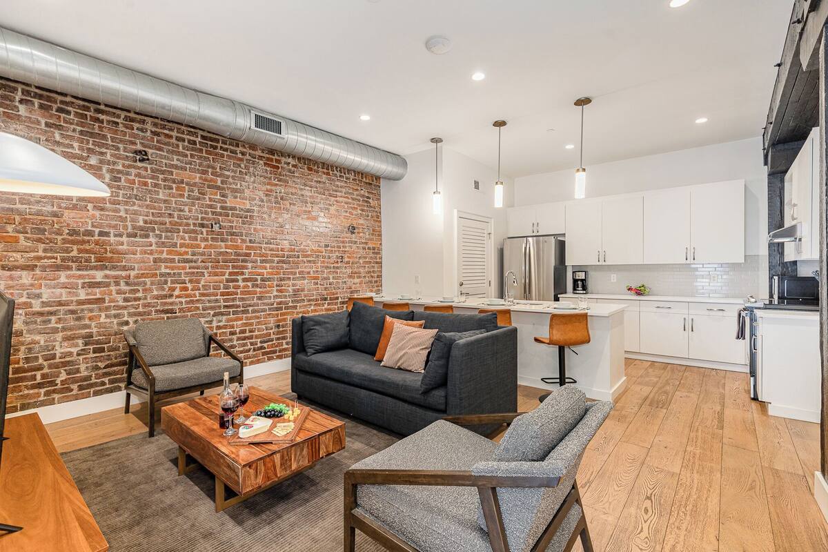 Ein modernes Wohnzimmer mit Backsteinwand, grauem Sofa und Couchtisch aus Holz.