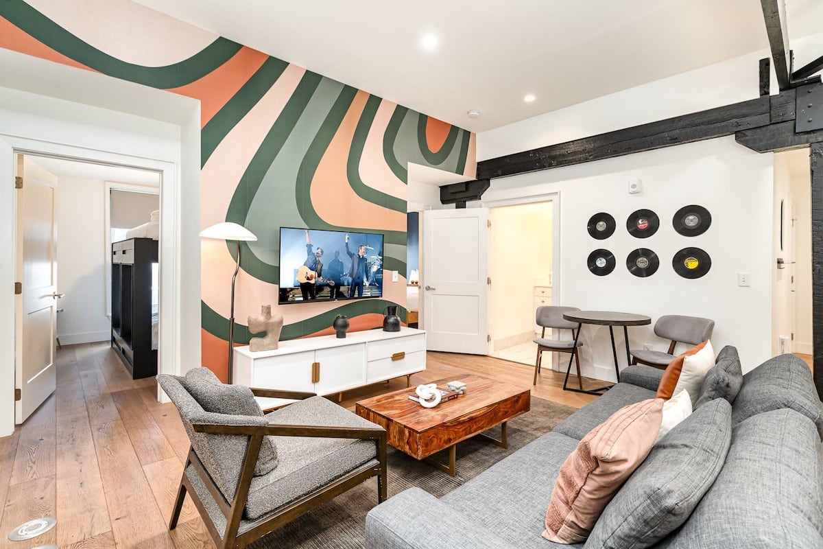 Ein modernes Wohnzimmer mit einer Couch, einem Sessel, einem Couchtisch und einem an der Wand montierten Fernseher.