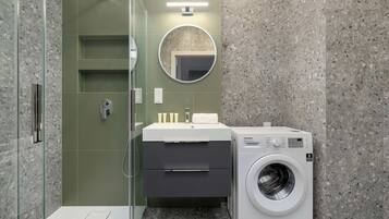 Un baño moderno con ducha envuelta en vidrio, un lavamanos con espejo y una lavadora de carga frontal.