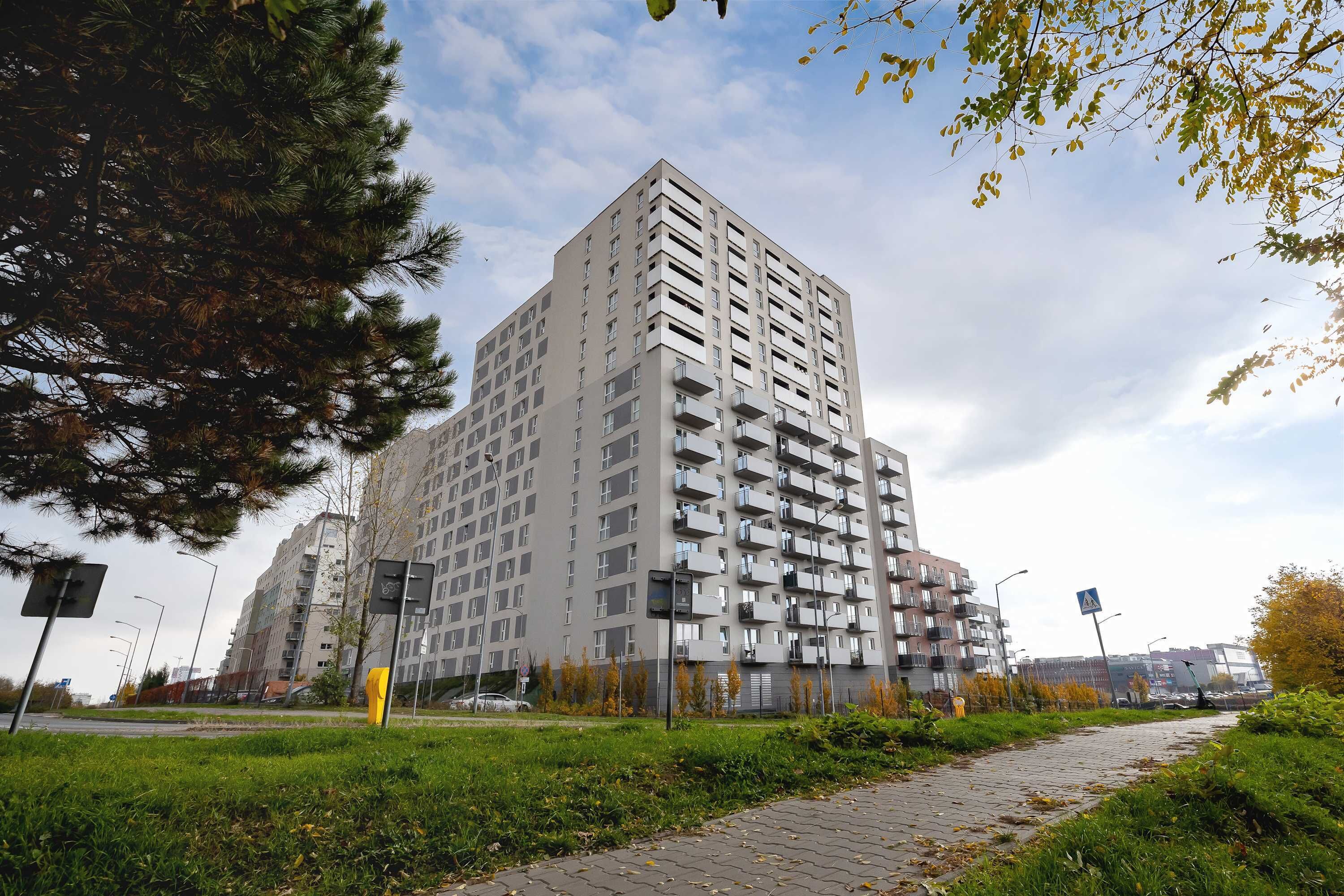 Um edifício residencial alto com várias varandas, cercado por vegetação e um caminho pavimentado.