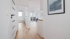 A modern, well-lit hallway with a framed picture on the wall, leading to a dining area with natural light from large windows. - Bright Apartment with Balcony | Parking, Workspace (Katowice)