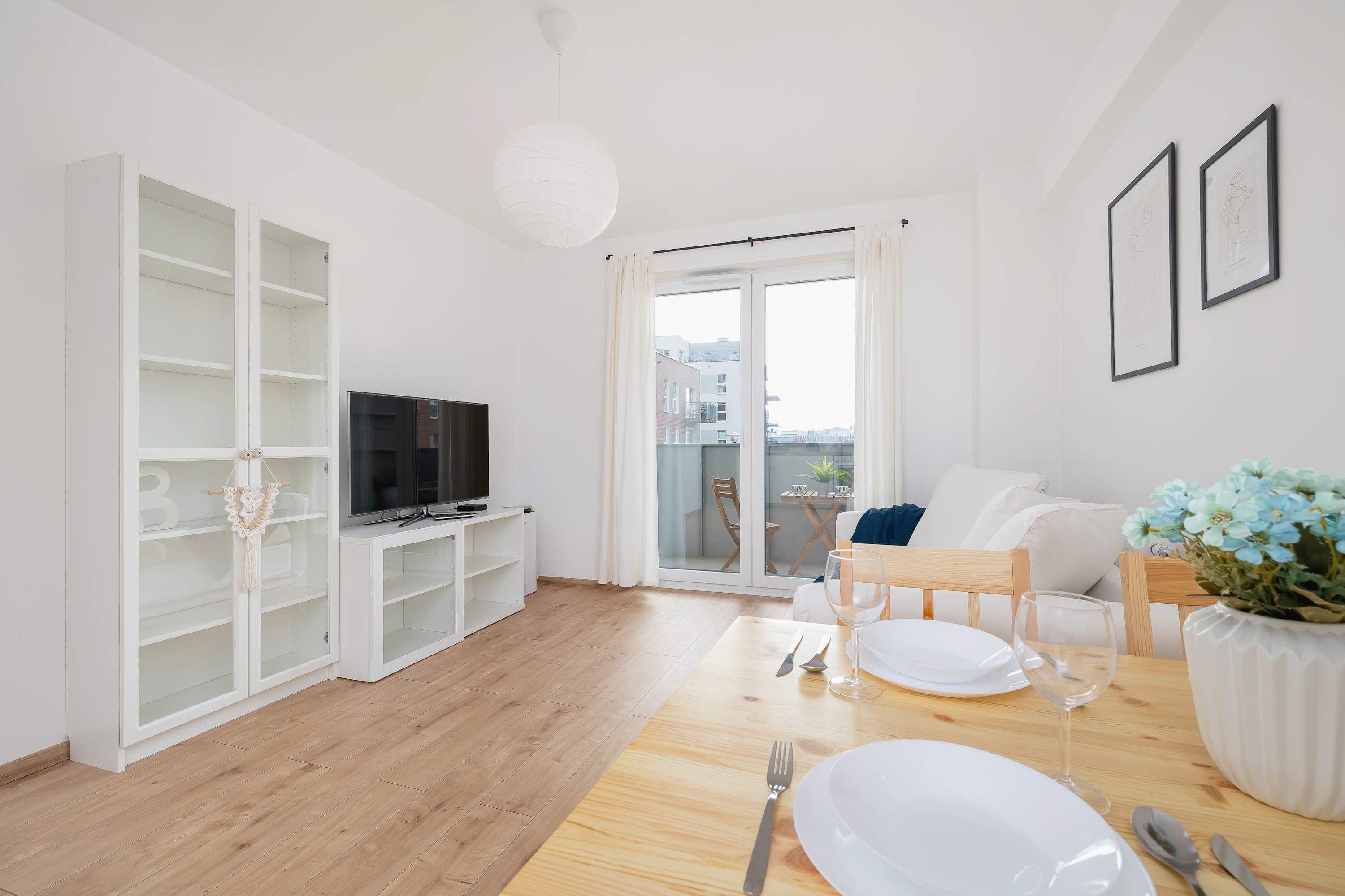 Ein modernes Wohnzimmer mit Holzboden, weißen Möbeln, einem Fernseher und einem Essbereich mit Tellern und Gläsern.