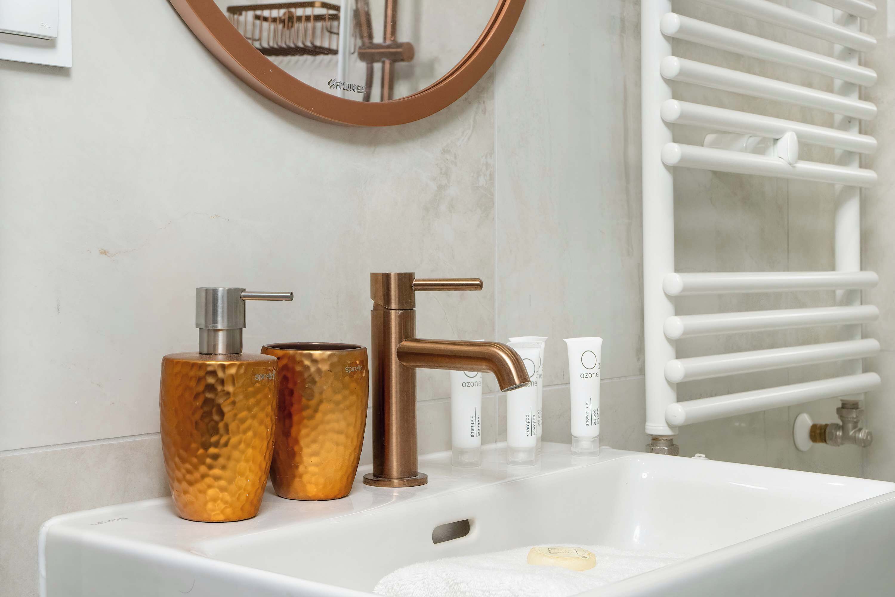 A bathroom with a white sink, two gold-colored soap dispensers, a copper faucet, and a white towel rack.