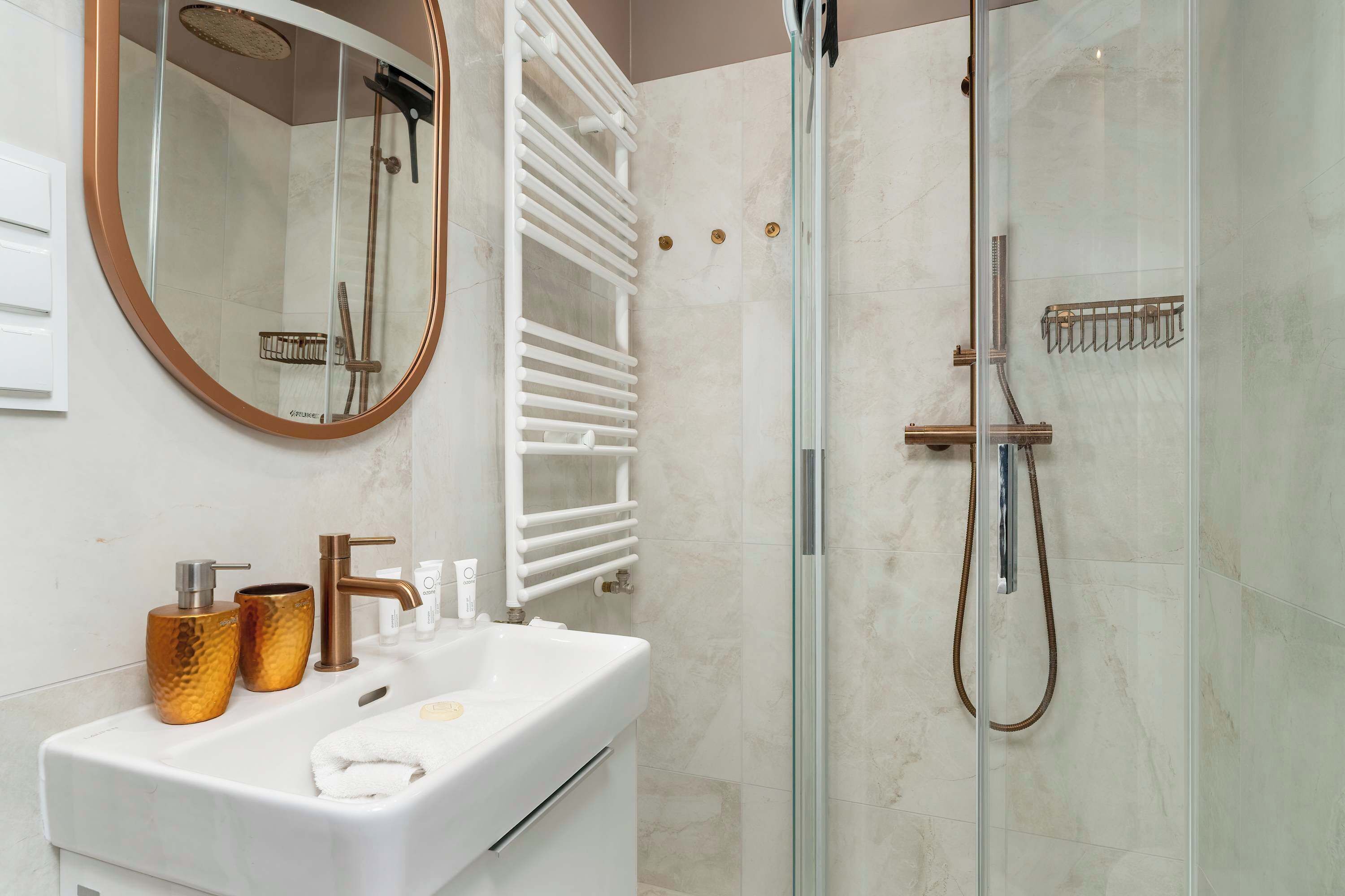 A modern bathroom with a glass-enclosed shower, a white sink with gold fixtures, and a large mirror.