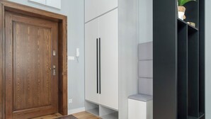 Un intérieur moderne avec une porte en bois, une armoire blanche, un banc gris et une étagère noire.